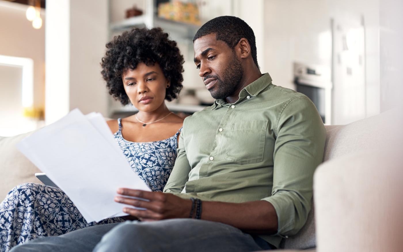 Two people sitting on a couch together as they look at a paper intently