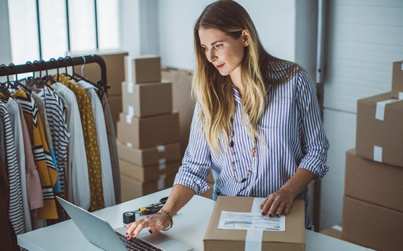 Woman scrolling on her computer while packaging a box