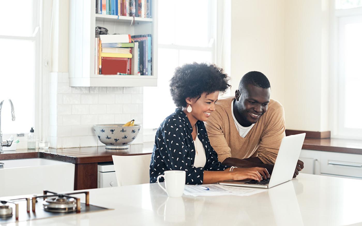 two people sitting at the dining room table looking at a laptop and smiling